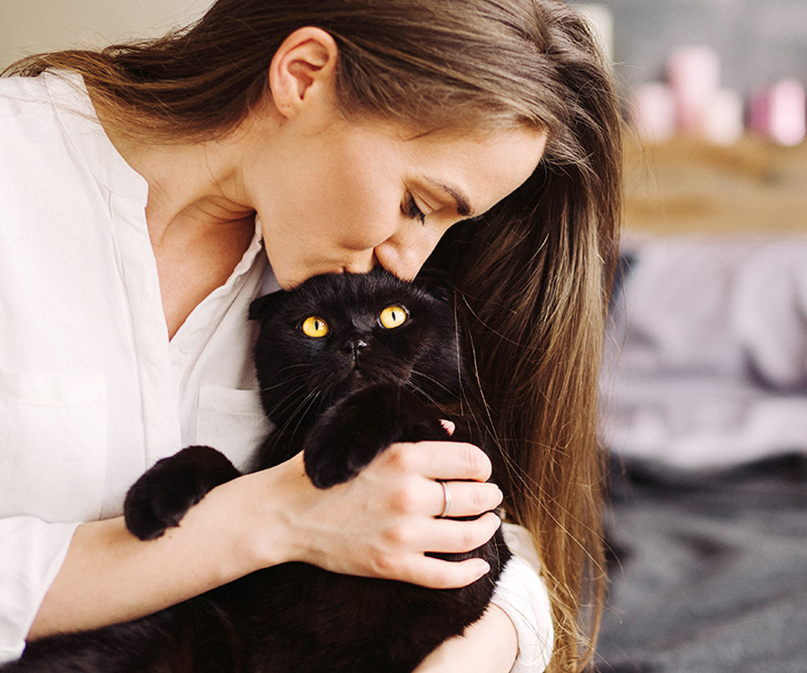 Happy young caucasian woman kissing and holding a black cat. Playing with pet at home.